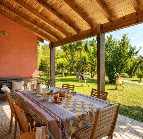 Terrazza in ombra al Maquis Plage con tavolo da pranzo, travi in legno e vista sul giardino a Poggio-Mezzana
