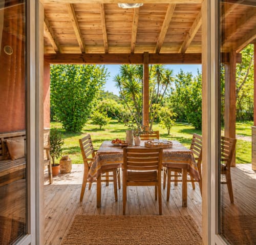 Terrazza coperta con tavolo in legno, sedie e vista sui rigogliosi giardini di Le Maquis Plage, Poggio-Mezzana