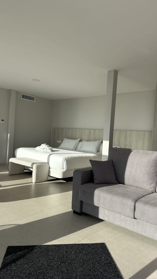 Modern bedroom at Otantus Maritimus hotel in Muros with gray upholstered seating, white bed, and minimalist décor