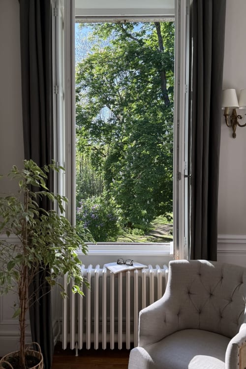 Elegant bedroom at La Maison 1680 in Couches with garden view through tall windows, upholstered chair, and greenery