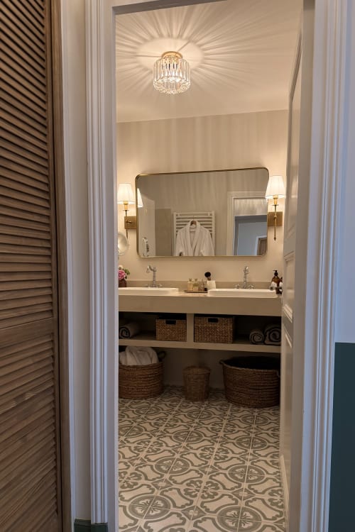 Elegant bathroom at La Maison 1680 with dual sinks, mirror, crystal fixture, and patterned tile floor