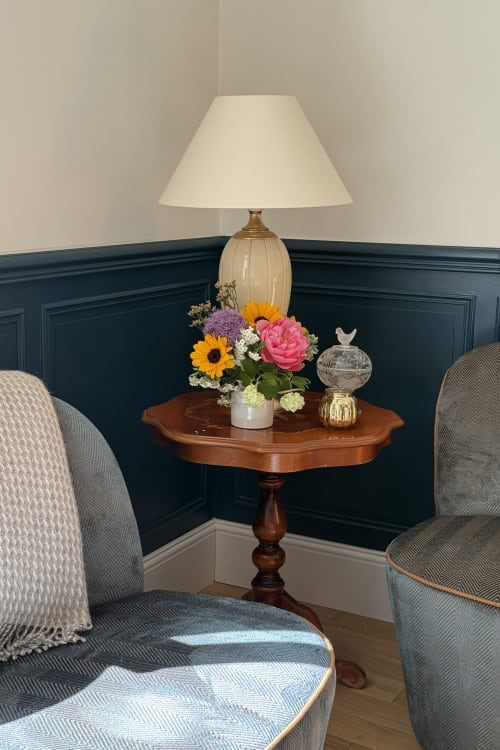 Elegant sitting area at La Maison 1680 with lamp, flowers on wooden table, and upholstered chairs