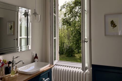 Modern bathroom at La Maison 1680 with dual vanity, mirror, and French doors opening to garden view in Couches