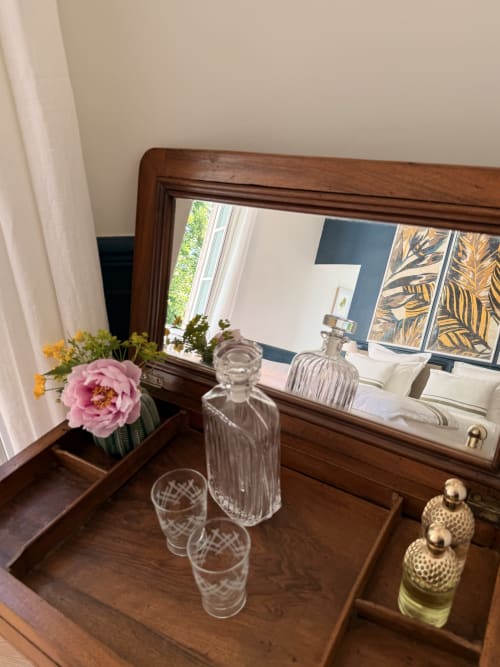 Wooden dresser with mirror displaying fresh pink flowers, crystal glasses, and perfume bottles in La Maison 1680 bedroom,