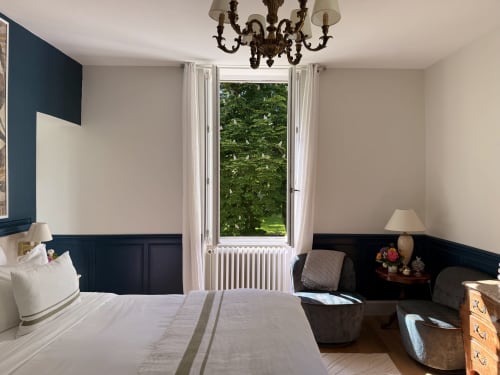 Elegant bedroom at La Maison 1680 with navy wainscoting, chandelier, and French doors opening to garden views in Couches