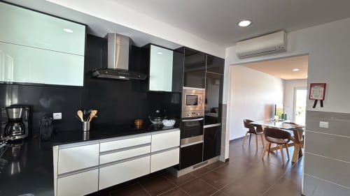 Cozinha moderna com armários preto e branco, eletrodomésticos em aço inoxidável e painel traseiro preto na vila Casa Cliff, Sesimbra