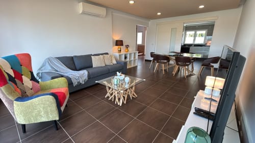 Sala de estar moderna na villa de Sesimbra com poltrona patchwork colorida, sofá cinzento, mesa de vidro e área de jantar com vista para piscina