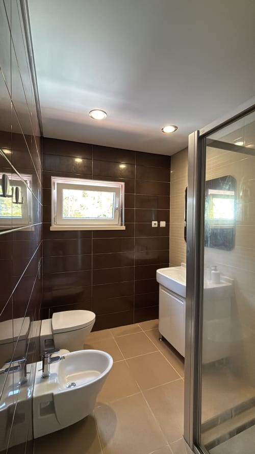Banheiro moderno da villa Casa Cliff em Sesimbra Sun Sea com azulejos escuros, pia branca, vaso sanitário, bidê e chuveiro tipo walk-in