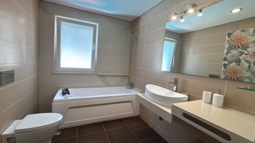 Banheiro moderno na villa Casa Cliff, Sesimbra com pia branca, banheira, vaso sanitário e espelho com iluminação