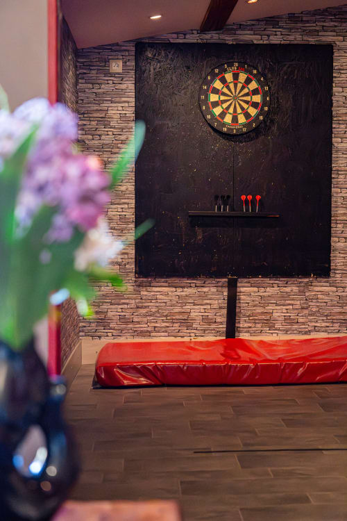 Salle de jeux de fléchettes au Domaine Sur-Valot avec sièges rembourrés rouges, murs en brique et cible à Beaubery