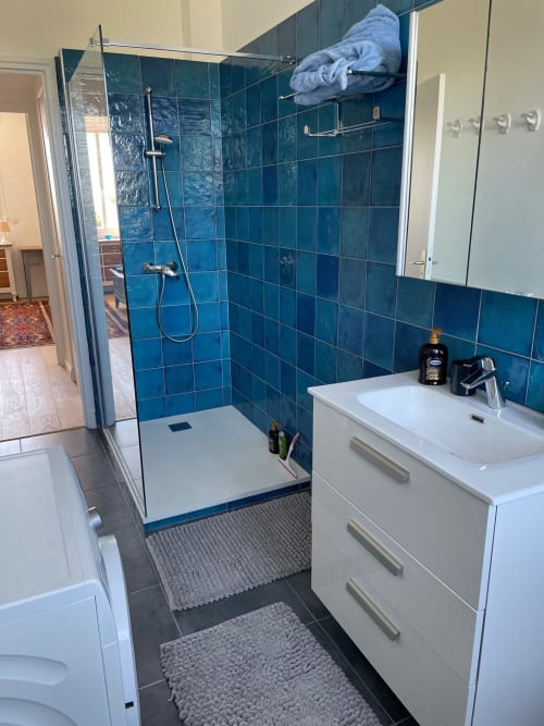 Modern bathroom with blue tile shower enclosure, white vanity sink, and dark flooring at Résidence Le Château Du Parc Santa