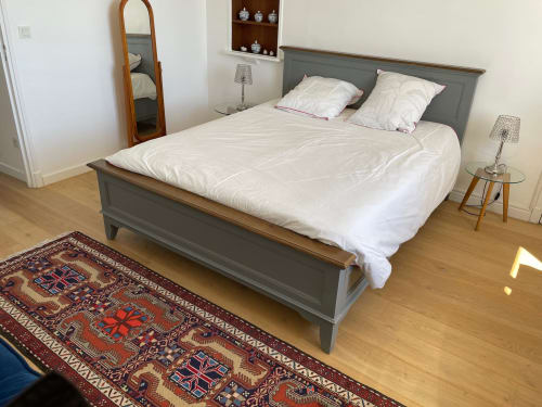 Spacious bedroom with gray bed frame, white linens, wooden mirror, and oriental rug in Saint Raphaël apartment