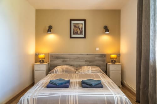 Chambre du gîte Domaine Sur-Valot avec tête de lit en bois, appliques murales et literie rayée à Beaubery, France
