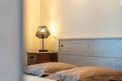 Chambre confortable du Domaine Sur-Valot avec lampe de table décorative sur table de nuit en bois et tête de lit rembourrée.