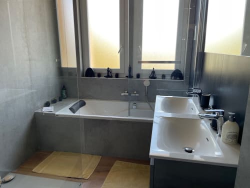 Modern bathroom with dual sinks, bathtub, and gray tile at Résidence Le Château Du Parc, Saint Raphaël