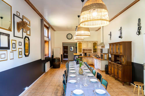 Salle à manger du Gîte L'Écurie au Domaine Sur-Valot avec table conviviale, luminaires suspendus tressés et accès à la cuisine