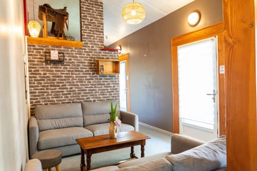Salon accueillant du Gîte L'Écurie, Domaine Sur-Valot avec canapé gris, table en bois, mur de briques et ambiance chaleureuse