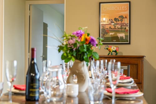 Élégante salle à manger du Domaine Sur-Valot avec table dressée, fleurs fraîches, bouteille de vin et affiche Charolles