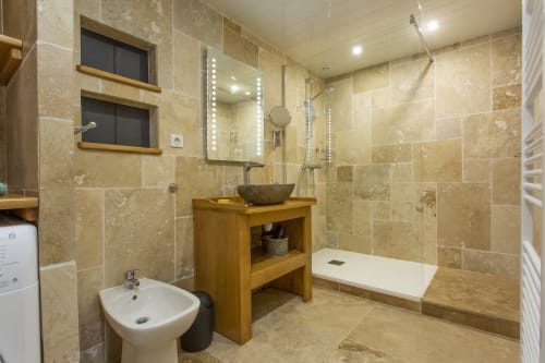 Salle de bains moderne au Domaine Sur-Valot avec carrelage en travertin, meuble-lavabo en bois, vasque, douche à l'italienne et miroir LED