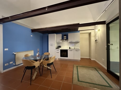 Modern open-plan loft apartment at Cinelli Apartment Vercelli with blue walls, white kitchen, dining table, and terracotta
