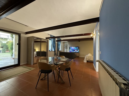 Modern loft apartment in Vercelli with open-plan living area, dining table, TV, dark wooden beams, and garden access
