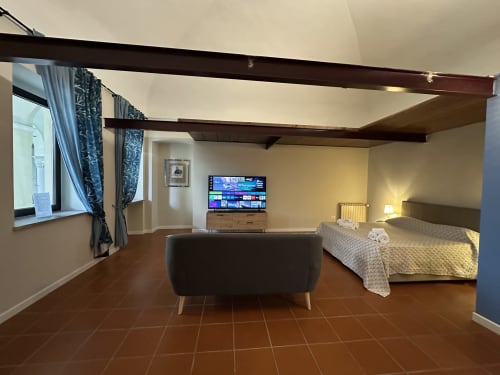 Spacious loft bedroom at Cinelli Apartment in Vercelli with TV, lounge seating, terracotta floors, and accessible amenities