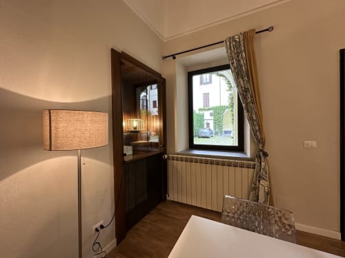 Vercelli apartment bedroom with window, radiator, floor lamp, and wooden door with glass panel