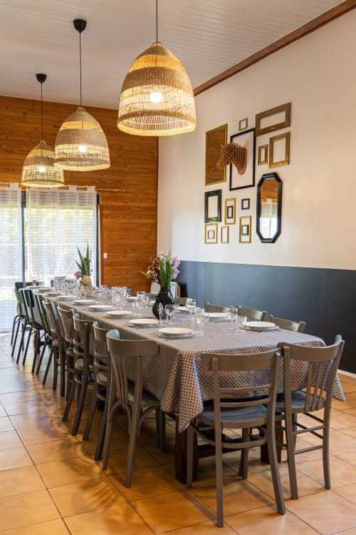 Élégante salle à manger du gîte Domaine Sur-Valot avec luminaires suspendus tissés, longue table et mur de galerie encadré
