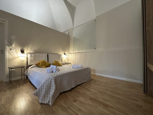 Modern loft bedroom at Cinelli Apartment in Vercelli with bed, golden pillows, wooden floors, and skylight ceiling