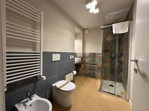 Modern bathroom at Cinelli Apartment in Vercelli with striped radiator, black tiles, toilet, sink, and glass shower enclosure