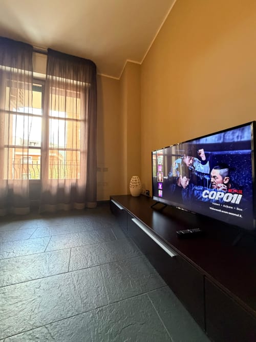 Modern apartment living room in Vercelli with flat-screen TV displaying Netflix, golden walls, dark flooring, and garden