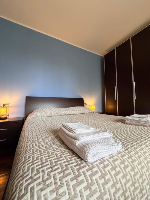 Spacious bedroom at Cinelli Apartment in Vercelli with dark wood bed, patterned bedding, white towels, nightstands with