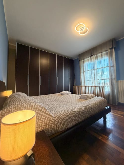 Spacious family bedroom at Cinelli Apartment in Vercelli with modern dark wardrobes, neon ceiling light, and garden views