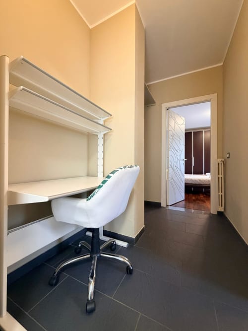 Modern home office nook in Cinelli Apartment with white desk, chair, and shelving in Vercelli, Italy