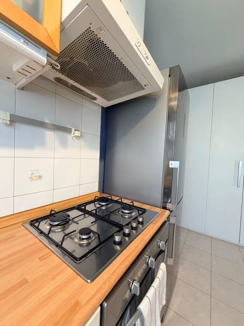 Modern kitchen with gas cooktop, range hood, and stainless steel refrigerator at Cinelli Apartment in Vercelli