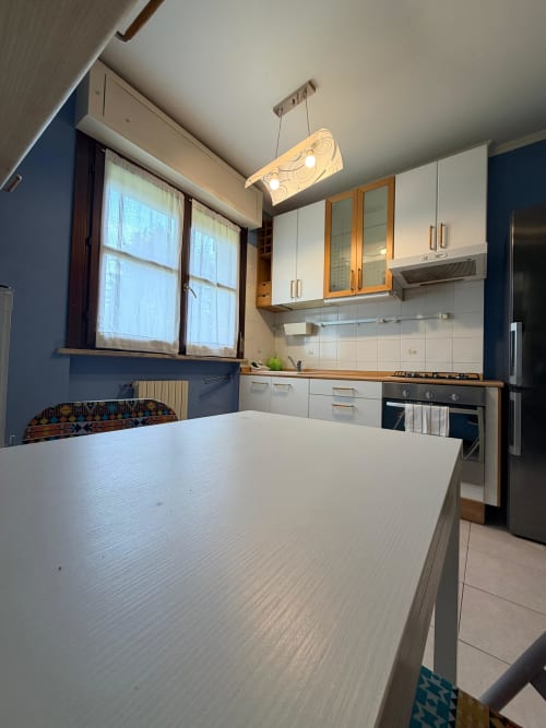 Modern kitchen in Cinelli Apartment, Vercelli with white cabinetry, dining table, and blue accent wall