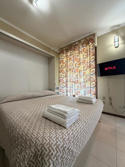 Modern bedroom at Cinelli Apartment Vercelli with double bed, white towels, patterned curtains, wall-mounted TV, and tile