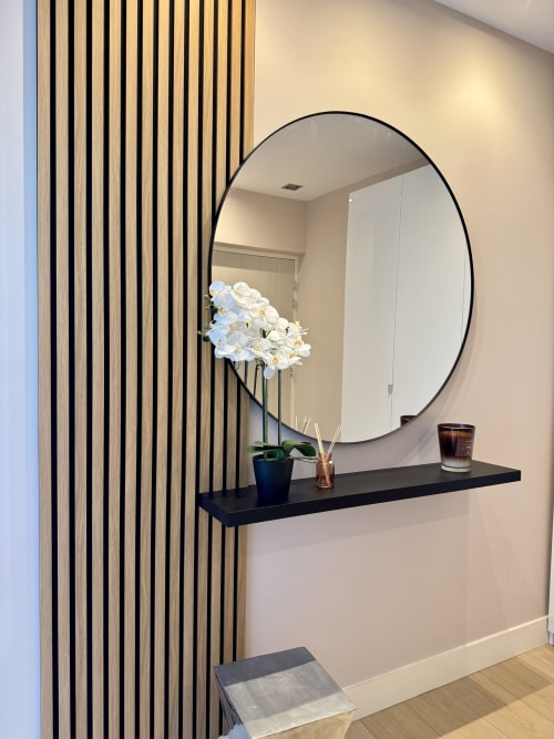 Entrée contemporaine de la location de vacances et séjour Eugénie avec miroir rond, orchidées blanches et mur à lames de bois à Ajaccio. 
