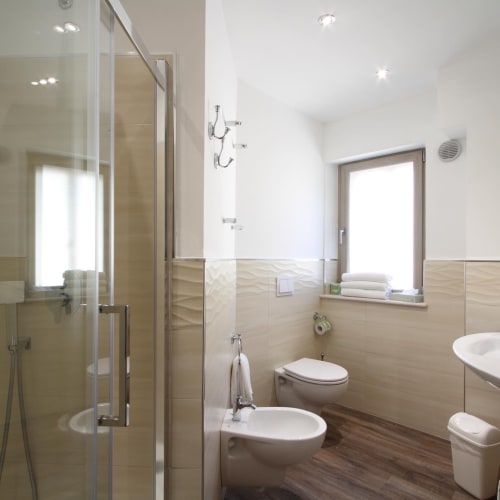 Modern bathroom in Il Viottolo junior suite, Roccaraso with glass shower, bidet, toilet, and window with natural light