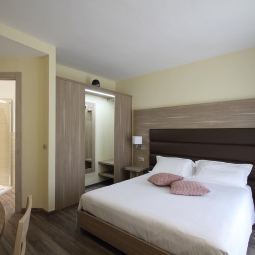 Modern hotel bedroom at Il Viottolo in Roccaraso with white bed, brown headboard, yellow walls, and wooden wardrobe.