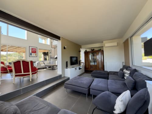 Salon contemporain de la villa SoleMare avec canapé anthracite, fauteuils rouges et vue sur le jardin, Alata