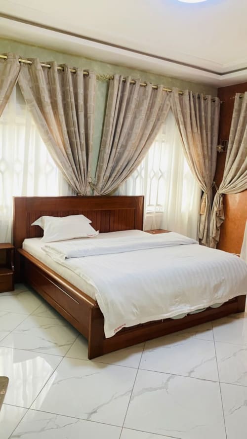 Chambre spacieuse du Kylian Appart Hotel avec lit en bois, draps blancs et élégants rideaux beige à Brazzaville
