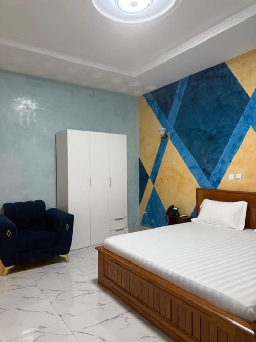 Chambre double luxe à l'hôtel Kylian Appart avec art mural géométrique bleu, lit en bois, armoire blanche et fauteuil
