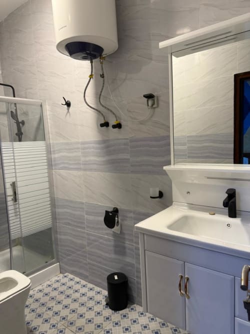 Salle de bain moderne du Kylian Appart Hotel Brazzaville avec vasque blanche, cabine de douche et carrelage à motifs