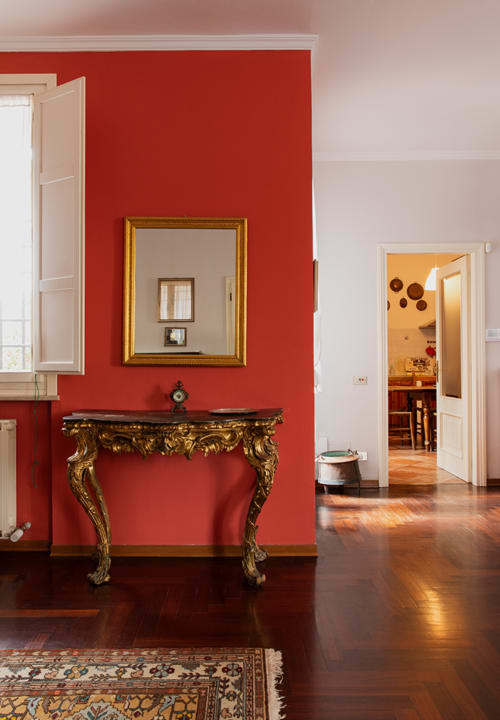 Elegant red hallway with ornate gold console table and mirror at Cristallo Apartment in Ravenna