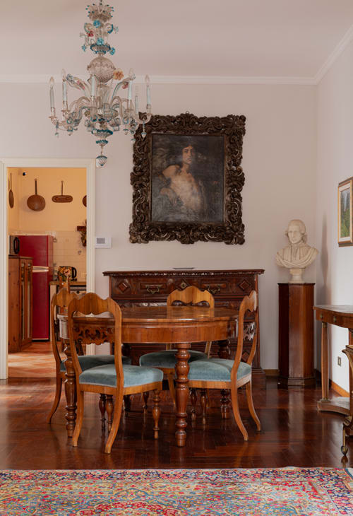 Elegant dining room at Cristallo Apartment in Ravenna with round table, wooden chairs, chandelier, and classical decor