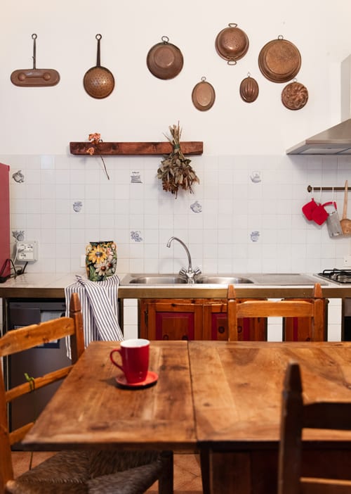 Rustic kitchen at Cristallo Apartment, Ravenna with copper cookware, wooden table, red mug, and white tile backsplash