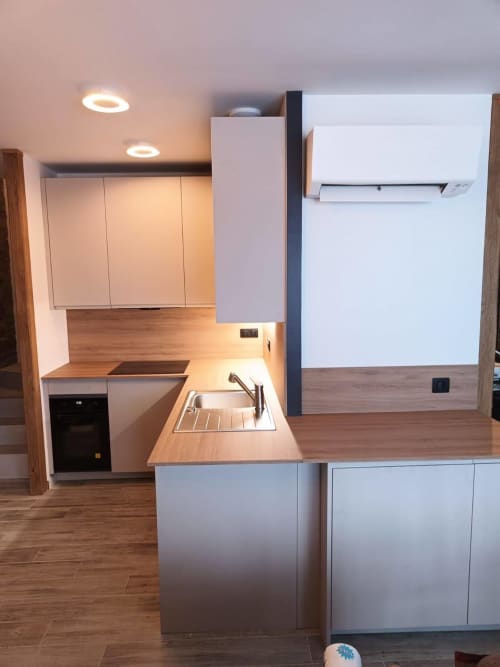 Cuisine moderne avec armoires blanches, plan de travail en bois, évier et appareils en acier inoxydable à CIRELINE-La Fontaine du Roy