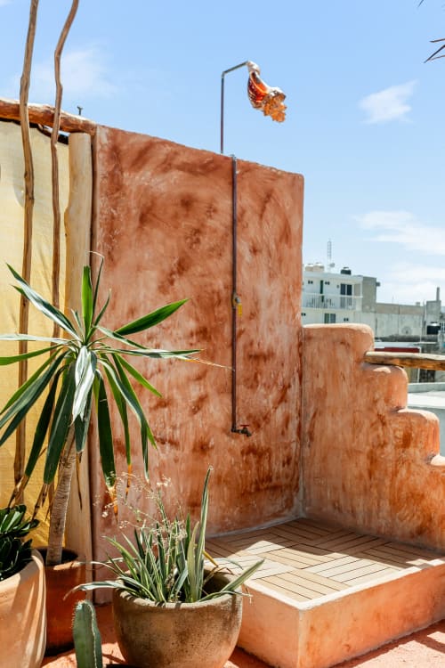 Beachfront cottage outdoor shower with terracotta walls, tropical plants, and ocean view at Isla Mujeres Realty