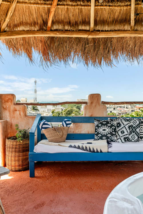Blue bed with colorful pillows on oceanfront terrace of Casa Amor cottage in Isla Mujeres, with thatched roof and city views